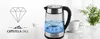 A glass electric kettle with blue illuminated water is shown on a white surface next to a white mug and a green plant. Náhled obrázku produktu
