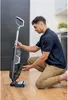 A man is kneeling on a wooden floor, interacting with a vacuum cleaner. Voir les images du produit
