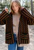 A young woman stands outdoors in a sandy area with trees in the background, wearing a patterned cardigan over a button-up shirt and jeans. Produktbild-Vorschau