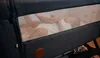 A baby lying in a crib with a hand gently touching its back. Produktbild-Vorschau