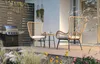 A patio set with two chairs and a table on a wooden deck, surrounded by plants. Náhled obrázku produktu