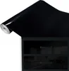 A roll of black glossy adhesive film is placed over a black cabinet with glass doors. Produktbild-Vorschau