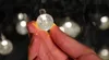 A hand holding a small, clear, spherical LED light bulb from a string of lights. Náhled obrázku produktu