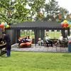 People enjoying a backyard gathering under a large tent, with a barbecue and seating area. Voir les images du produit