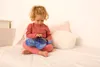 A young child sits on a bed holding a blue stuffed turtle that projects lights. Voir les images du produit