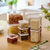 A collection of clear plastic food storage containers filled with various dry goods, arranged on a wooden table. Produktbild-Vorschau