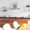 A modern kitchen with white brick walls, stainless steel appliances, and wooden cabinets. The image shows a range hood, shelves with kitchenware, and dining chairs in the foreground. Produktbild-Vorschau