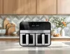 A double-chamber air fryer is displayed on a kitchen counter, with kitchen cabinets and a backsplash in the background. Podgląd zdjęcia produktu