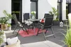An outdoor patio set with chairs and a table on a tiled floor, surrounded by plants. Produktbild-Vorschau