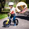 A young boy riding a balance bike on a paved path in a park. Produktbild-Vorschau