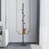 A black coat rack with a tan handbag hanging on it, placed in a room with a white sofa and a decorative wall. Produktbild-Vorschau