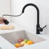 A hand is holding a black kitchen faucet sprayer, rinsing fruit in a sink. Produktbild-Vorschau