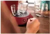 A person's hand is operating a red coffee machine with two clear glasses on it. Produktbild-Vorschau