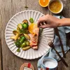 A person is garnishing a plate of salmon and vegetables with herbs. Voir les images du produit