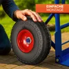 A person's hand is resting on a wheel of a blue hand truck, with a green grassy background and a paved surface in the foreground. Produktbild-Vorschau