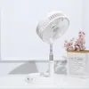 A white portable fan is displayed on a white desk, with a small bouquet of pink flowers in a paper bag to the right. Náhled obrázku produktu