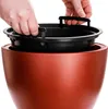 Hands holding a black planter insert over a brown planter. Produktbild-Vorschau