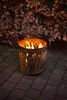 A fire pit with flames burning sits on a paved patio in front of a bush with dry leaves. Produktbild-Vorschau