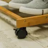 A close-up view of a mobile phone stand made of bamboo, showing its wheels and a portion of a shoe resting on it. Produktbild-Vorschau