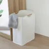 A white laundry basket with wooden handles and a gray towel draped over the side, placed on a wooden floor next to a wooden partition. Produktbild-Vorschau