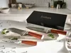 A set of three knives with wooden handles are displayed on a cutting board, with a black gift box in the background. Náhled obrázku produktu