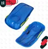 A collage of two blue sleds with green handles, one slightly above and to the left of the other. There are also some abstract red and black shapes in the top left and bottom right corners. Voir les images du produit