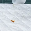 A close-up of a white quilted mattress protector with a liquid being poured onto it. Náhled obrázku produktu