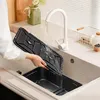 A person is rinsing a black air fryer basket under a white faucet in a kitchen sink. Produktbild-Vorschau