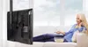 A woman is relaxing on a couch watching TV, which is mounted on a ceiling bracket. Produktbild-Vorschau