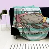 A blanket with a Pusheen cat design is draped over a black sofa. Produktbild-Vorschau