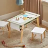 A child's activity table with a roll of paper and art supplies, set up on a rug with a toy train track nearby. Produktbild-Vorschau