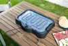 An electric grill on a wooden table outdoors, with food items nearby. Náhled obrázku produktu