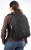 A woman wearing a brown shirt and blue jeans is seen from the back, wearing a black backpack. A blue water bottle is attached to the side of the backpack. Náhľad obrázku produktu