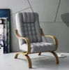 A grey armchair with wooden armrests and legs, placed on a light grey floor against a grey wall with geometric patterns. Podgląd zdjęcia produktu