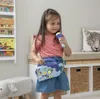 A young girl is holding a toy karaoke boombox and microphone in a room with bookshelves and storage. Anteprima dell’immagine prodotto