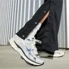 A person wearing black pants with snap buttons and white socks, showing off a pair of white and silver Nike sneakers. Produktbild-Vorschau