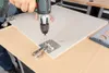A person is using a drill to attach a hinge to a cabinet door. Voir les images du produit
