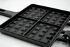 A close-up, angled view of a black cast iron waffle maker with a handle, set against a white background. Produktbild-Vorschau
