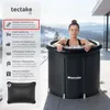 A woman is sitting in a portable ice bath outdoors with a snowy mountain landscape in the background. Náhled obrázku produktu