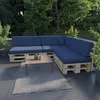 A sectional outdoor sofa made of pallets with dark blue cushions and a coffee table on a deck, surrounded by greenery. Produktbild-Vorschau