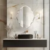 A modern bathroom vanity with a black sink, gold faucet, and a decorative silver mirror above it. The wall is covered in marble-like tiles. Anteprima dell’immagine prodotto