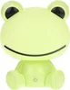 A light green, cartoon-like frog-shaped desk lamp with black eyes and a curved black mouth. It is sitting with its legs tucked in front of it, and there is a power button symbol on its lower body. Náhľad obrázku produktu