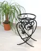 A black metal plant stand is shown next to a potted plant. Náhled obrázku produktu