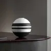 A spherical vase with black and white stripes sits on a dark, polished surface. Náhľad obrázku produktu