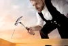 A craftsman is shown hammering a nail into a wooden beam against a backdrop of a colorful sky. Produktbild-Vorschau