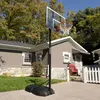 A portable basketball hoop is set up on a driveway in front of a house. Produktbild-Vorschau