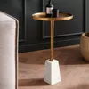 A small round side table with a gold top and a marble base, placed next to a sofa. Podgląd zdjęcia produktu