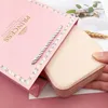 A hand is holding a small, rose-gold colored jewelry case that is partially inside a pink gift bag with 'PRINCESS' written on it. Produktbild-Vorschau