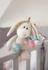 A plush donkey toy is hanging on the railing of a crib. Podgląd zdjęcia produktu