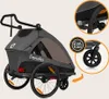 A gray child trailer with two wheels and a handle, shown from the side. Inset images highlight the EVA foam material and a close-up of the wheel. Produktbild-Vorschau